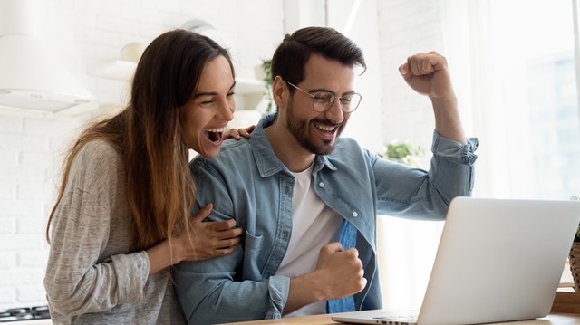 Overjoyed,Millennial,Couple,Sit,At,Desk,Look,At,Laptop,Screen
