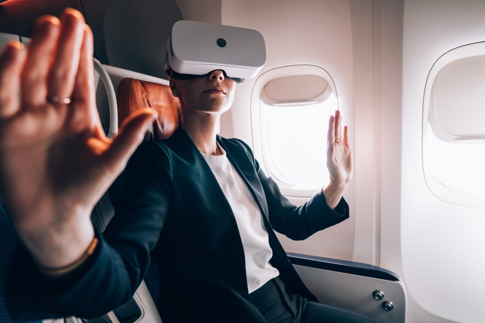 Female passenger in formal clothing spending flight time for creating 3d dimension projection in simulation cyberspace from digital VR goggles, woman in digital glasses gesturing haptic reality